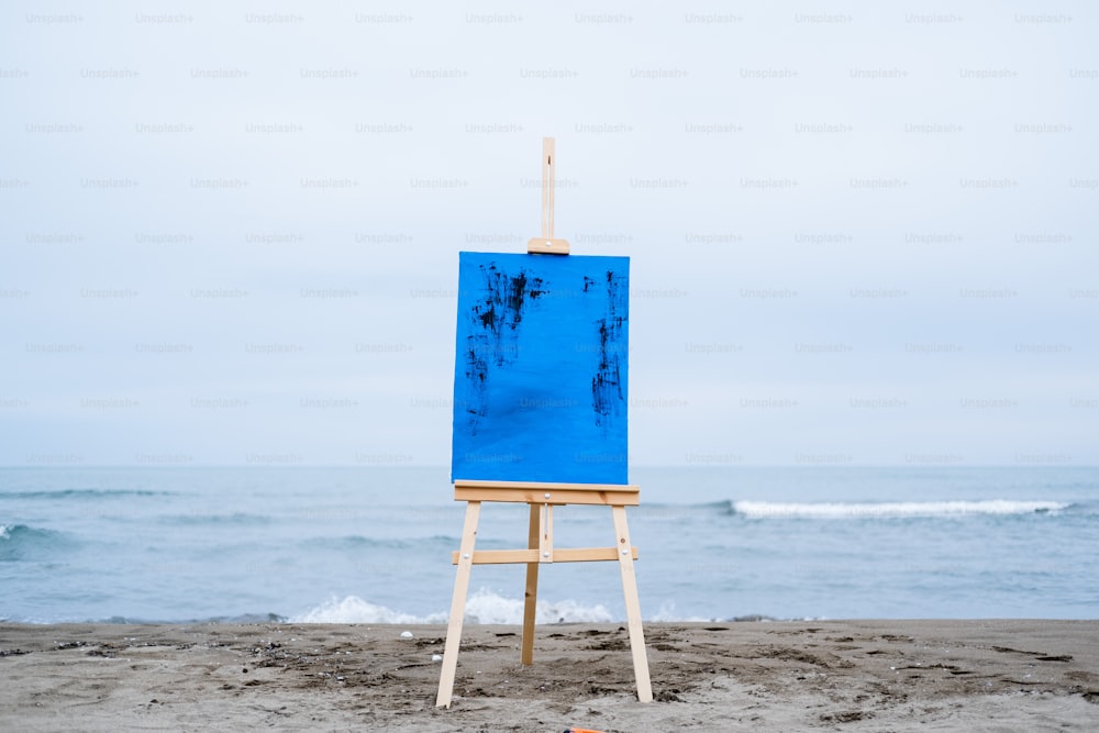 a blue easel sitting on top of a sandy beach