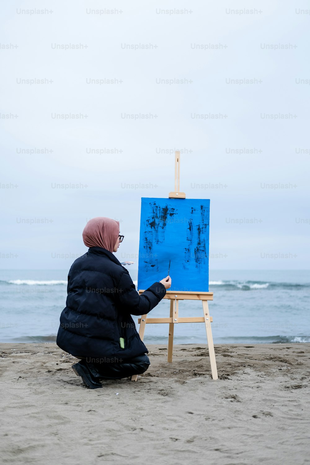 Eine Person, die vor einem Gemälde auf einer Staffelei sitzt