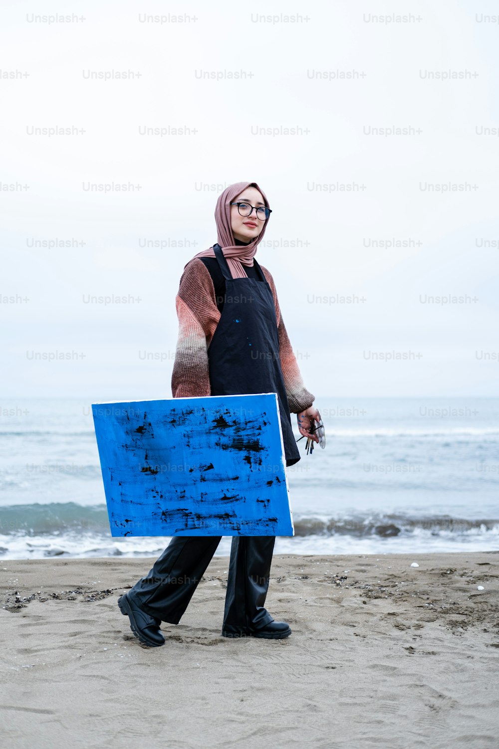 a woman walking on a beach holding a blue board