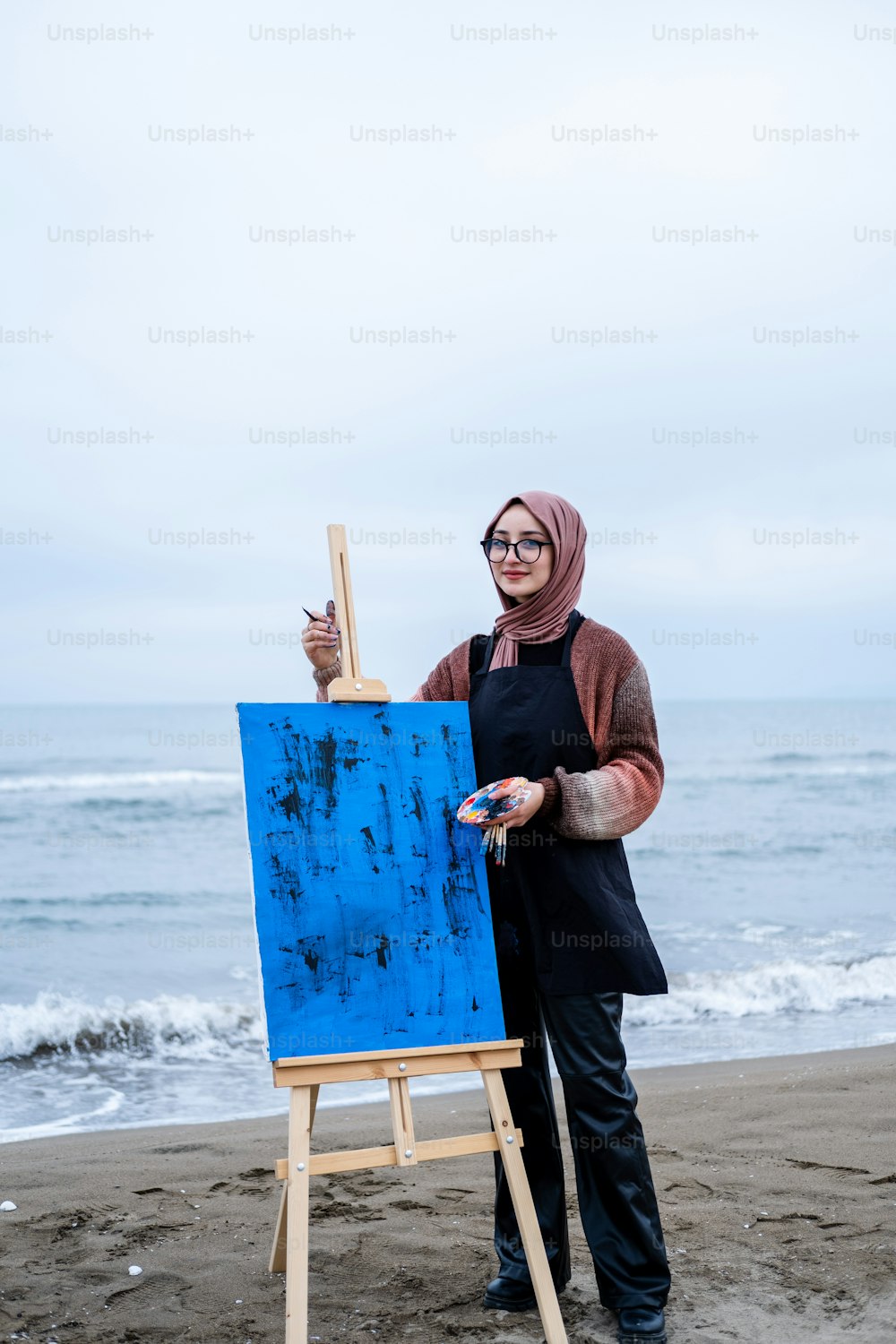 a woman standing on a beach next to an easel