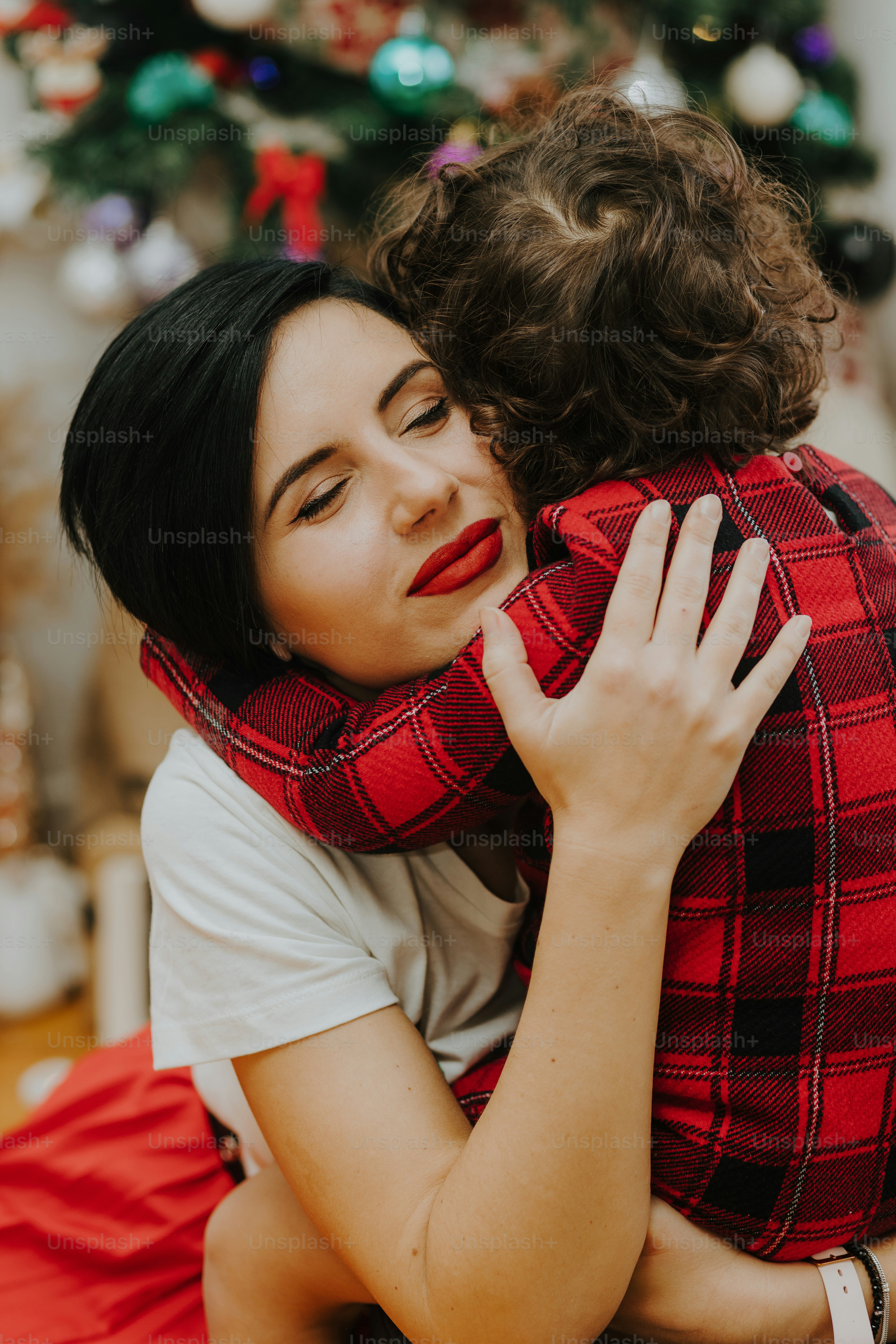 a woman hugging a child in front of a christmas tree