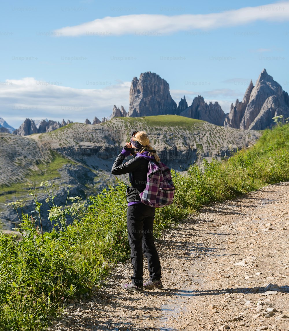 Una mujer parada en un camino de tierra junto a una exuberante ladera verde