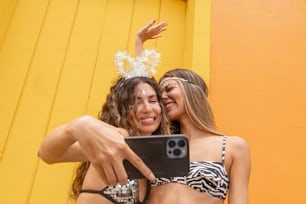 two women taking a selfie in front of a yellow wall