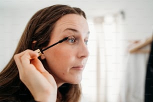 a woman is putting mascara on her face