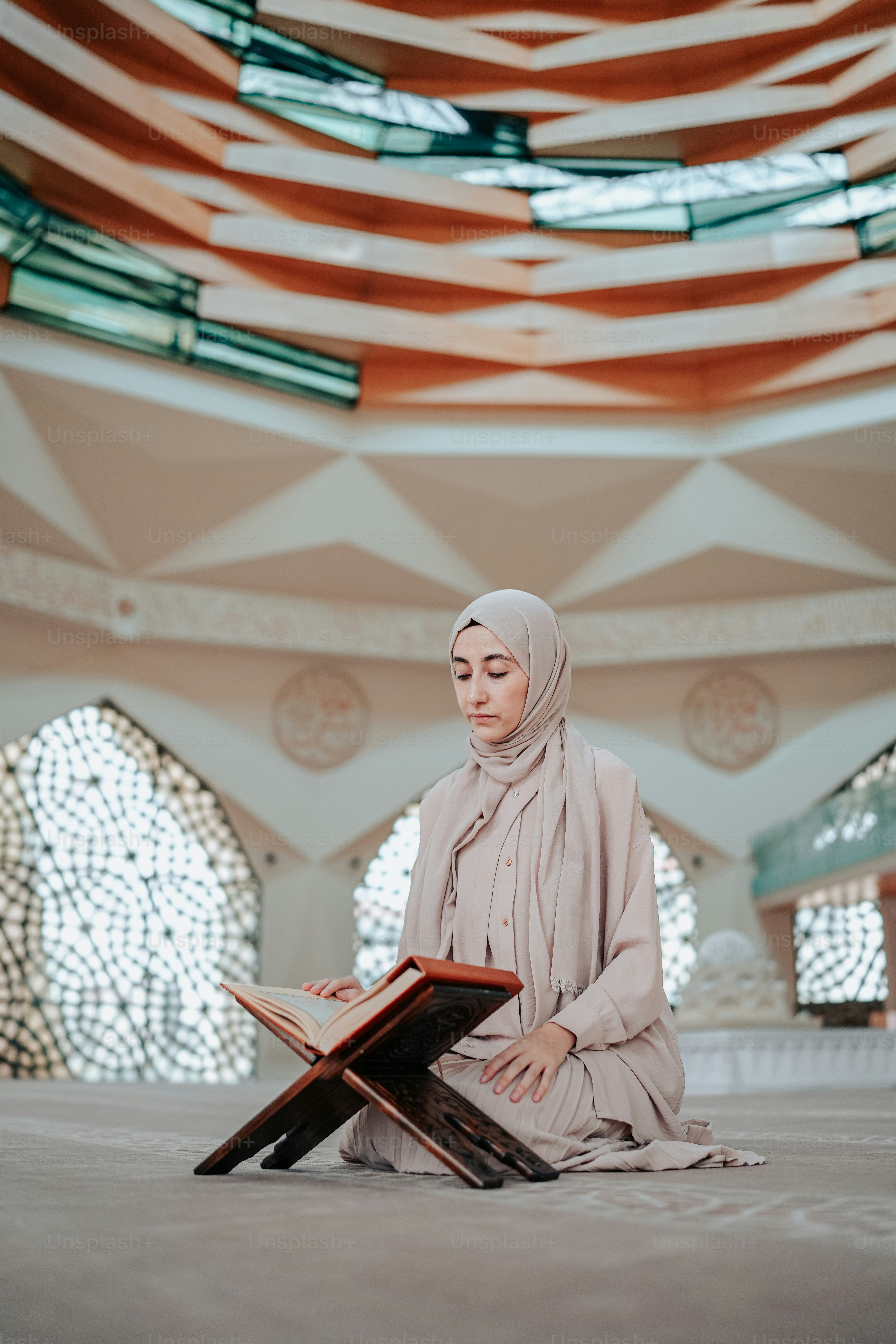 Seorang wanita berjilbab duduk di lantai membaca buku