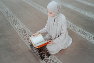 a woman in a hijab sitting on a rug reading a book