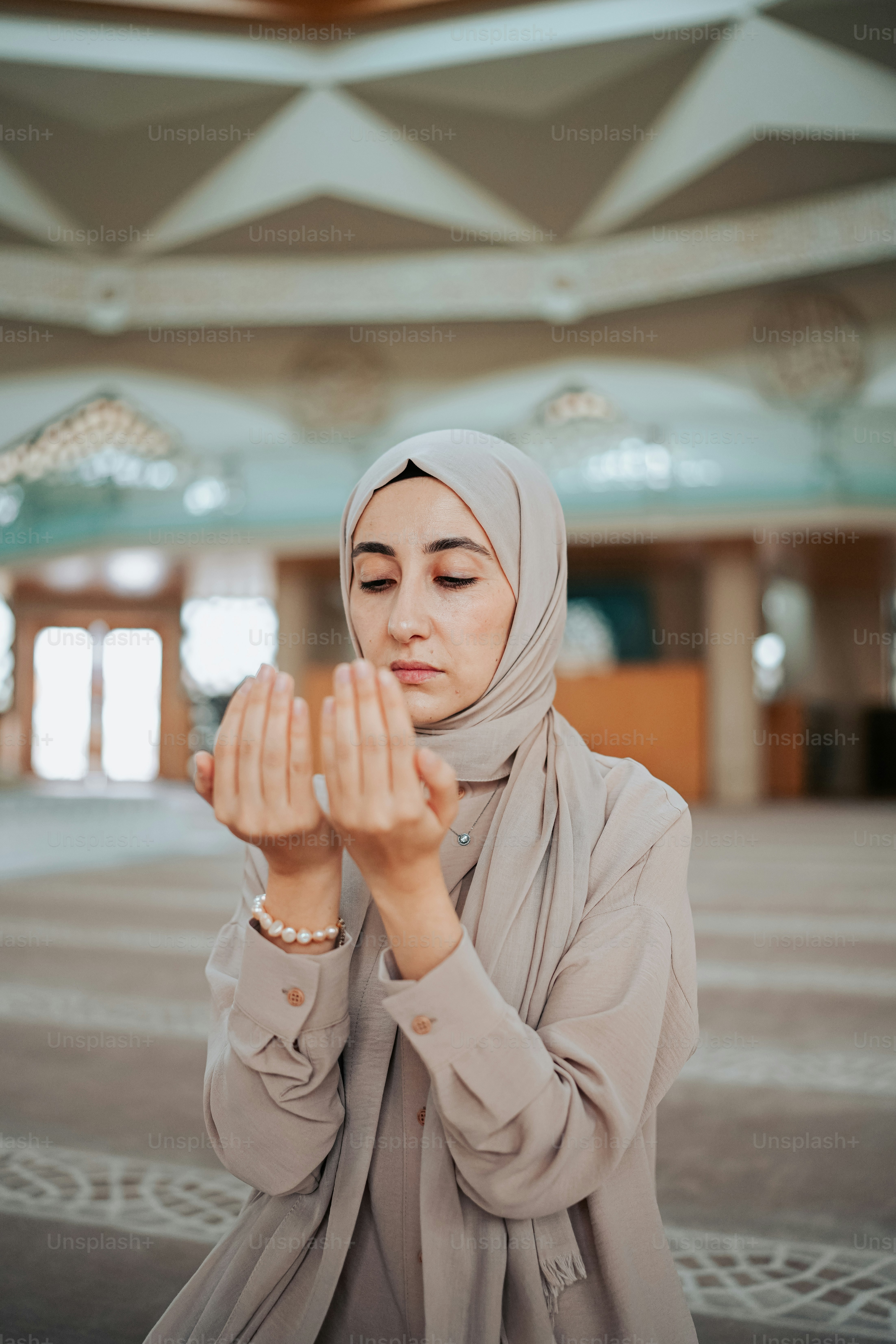 Seorang wanita berjilbab berjilbab berdoa di ruangan besar