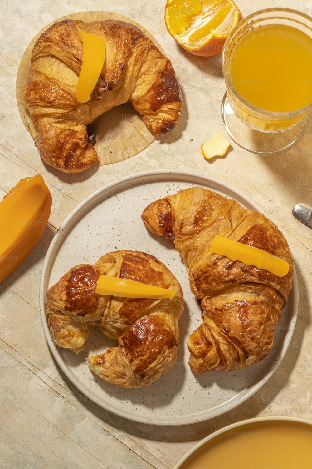 オレンジジュースのグラスの隣の皿にチーズとクロワッサン