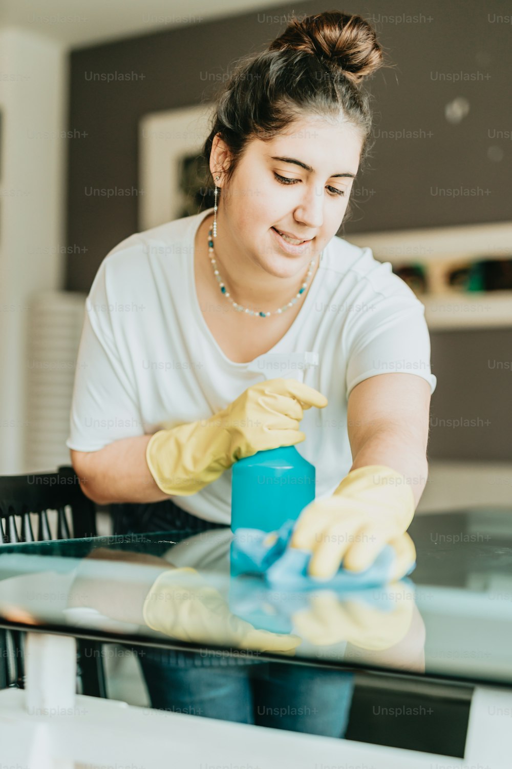 a woman in a white shirt and yellow gloves cleaning a table