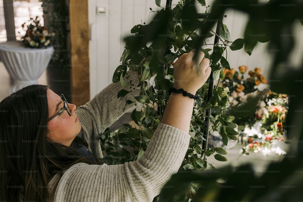Una mujer con un suéter blanco está recortando una planta