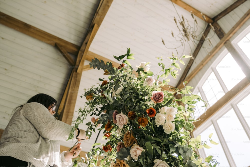Una mujer de pie junto a un jarrón alto lleno de flores
