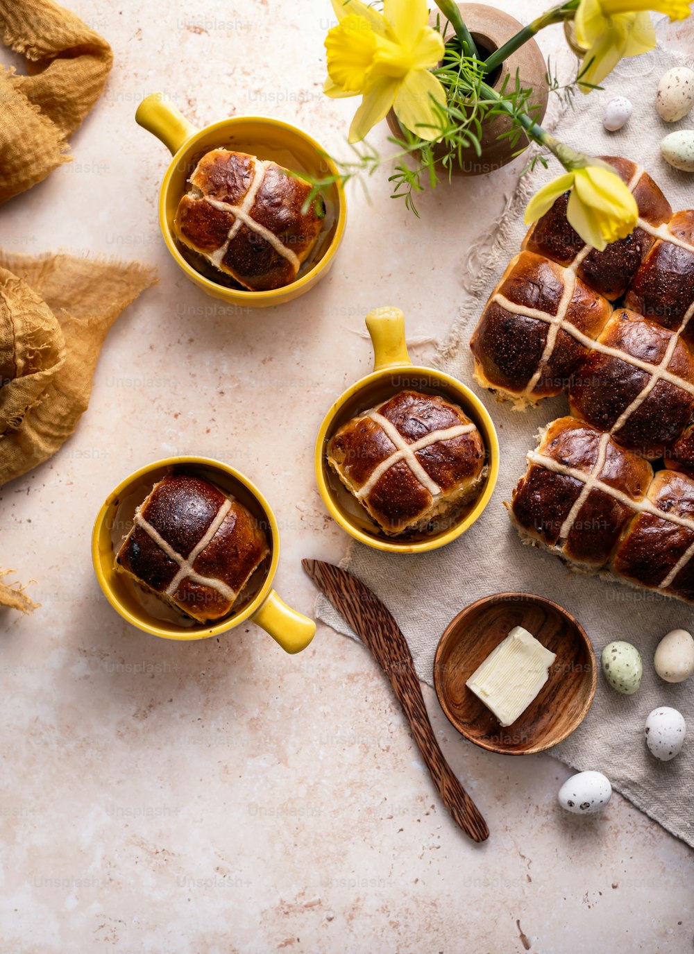 a table topped with yellow cups filled with hot cross buns
