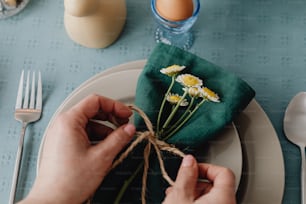 uma pessoa amarrando um guardanapo com margaridas em um prato