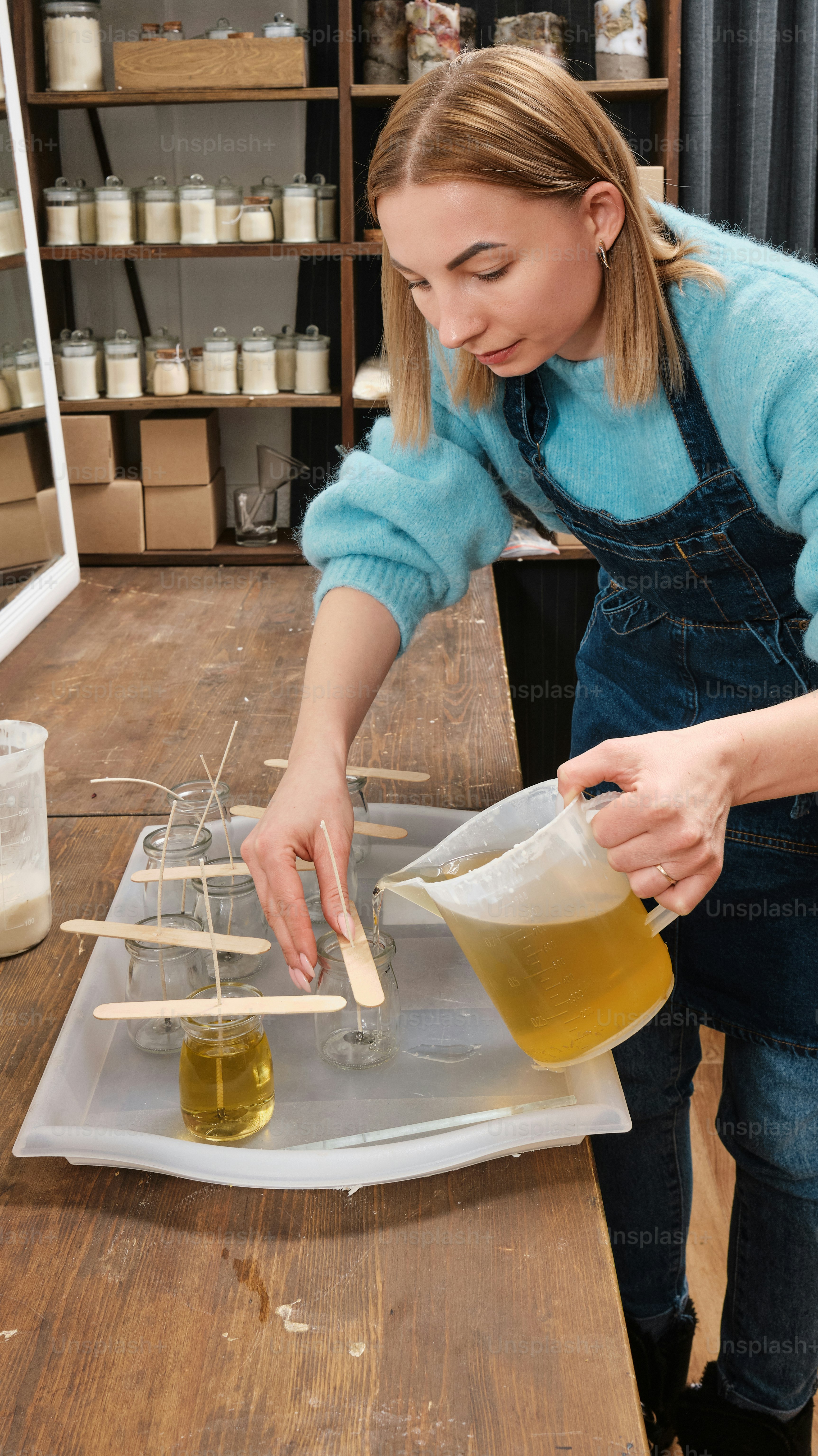 uma mulher em um suéter azul e macacão derrama um líquido em um recipiente
