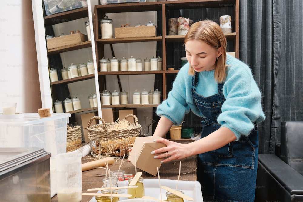 a woman in overalls and a blue sweater is putting something in a box