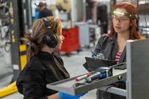 duas mulheres em uma fábrica conversando uma com a outra