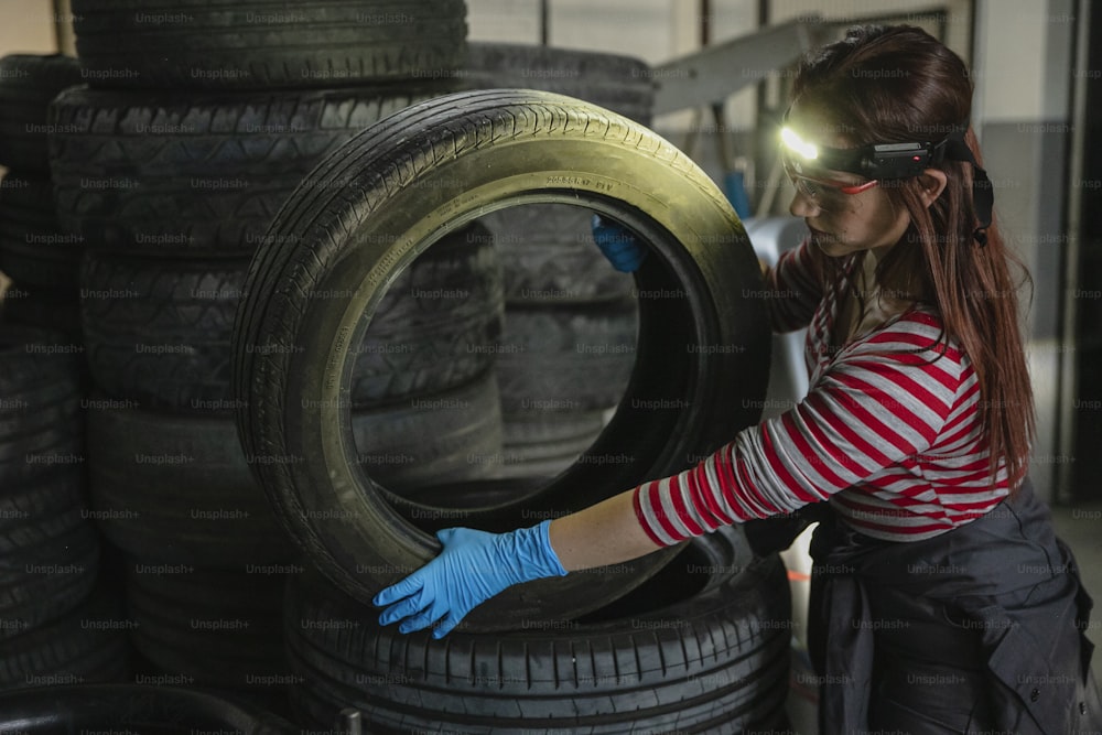Una mujer con camisa a rayas y guantes azules trabajando en un neumático