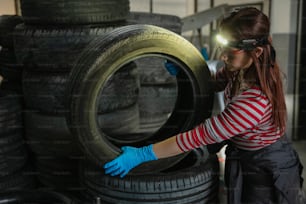 a woman in striped shirt and blue gloves working on a tire