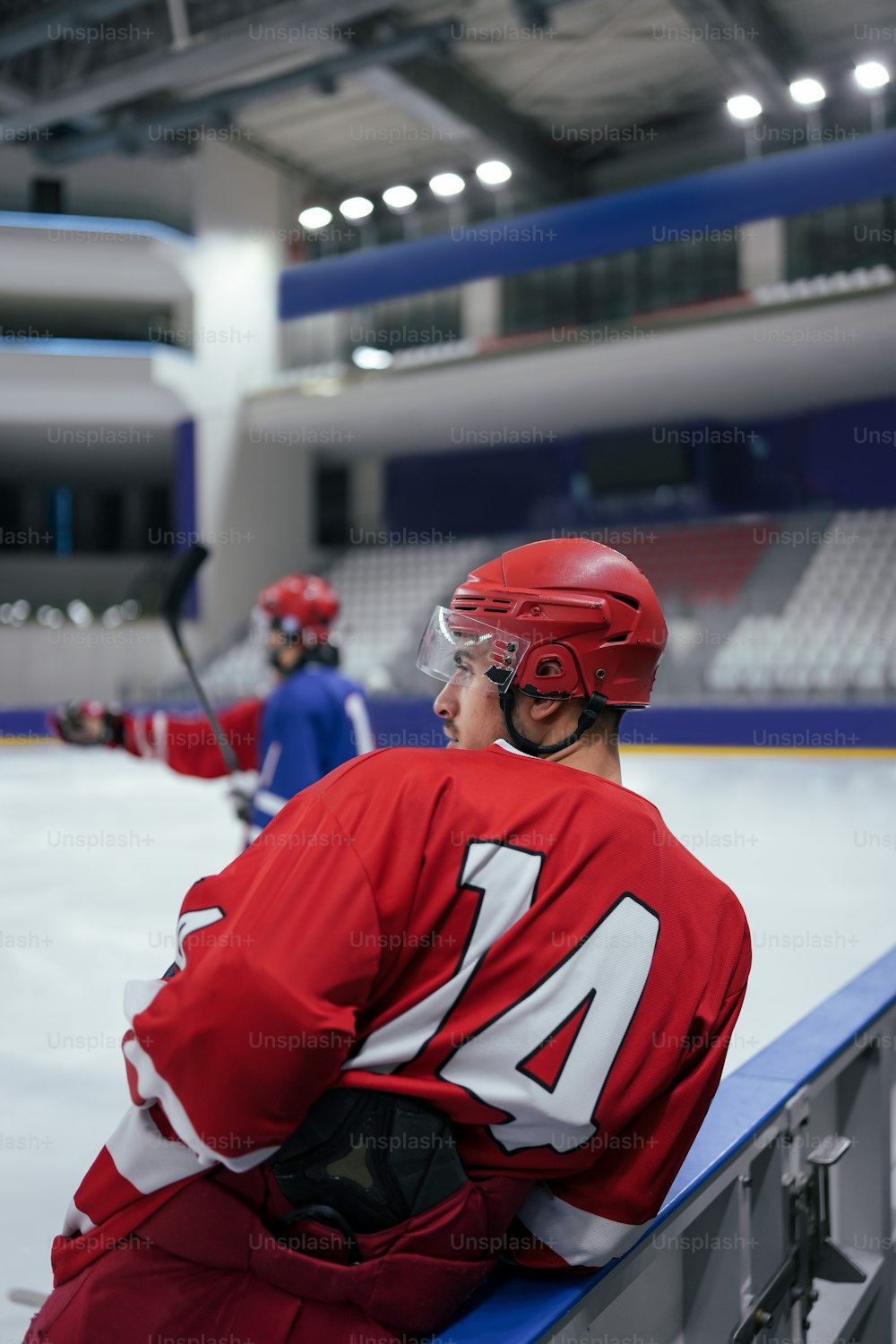 a man sitting on a bench wearing a red hockey uniform