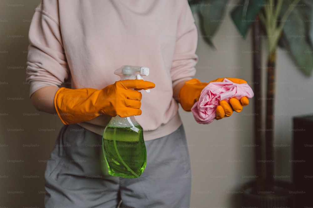 eine Person mit orangefarbenen Handschuhen, die eine Flasche Reiniger hält