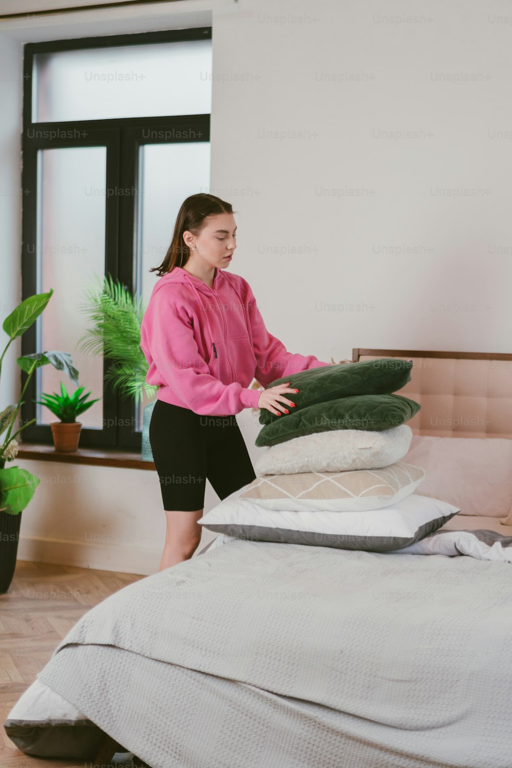 a woman standing next to a pile of pillows on top of a bed