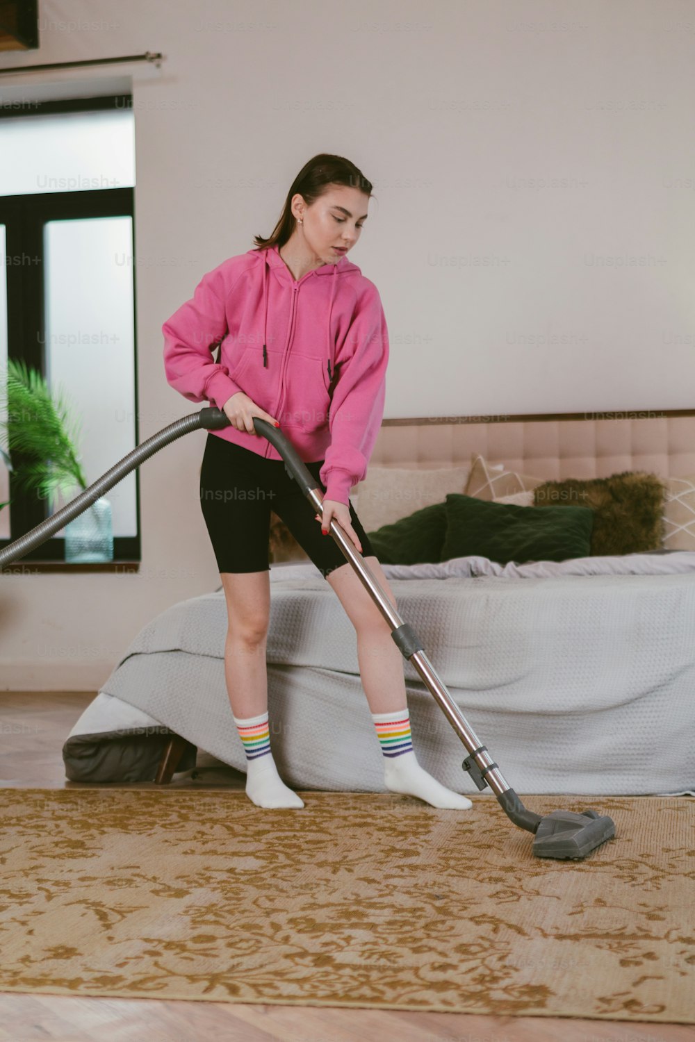 ベッドを掃除機で掃除するピンクのパーカーを着た女性