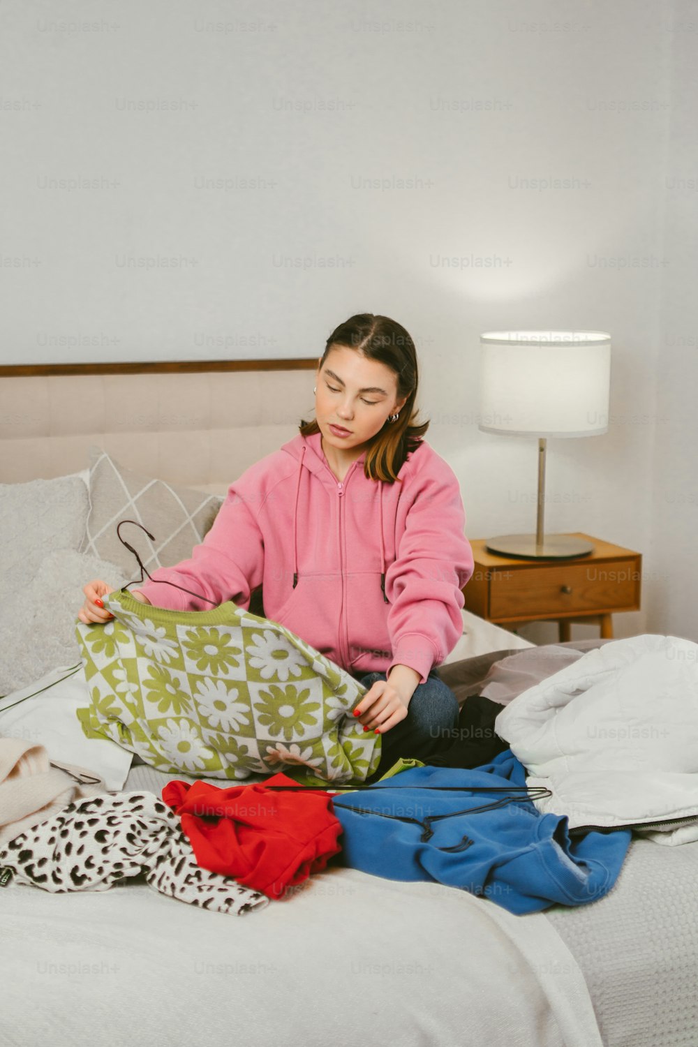 a woman sitting on a bed with a pile of clothes