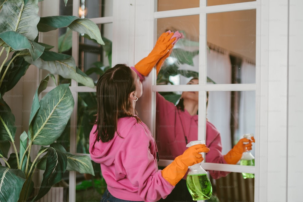 Una mujer con una camisa rosa y guantes naranjas limpiando una ventana