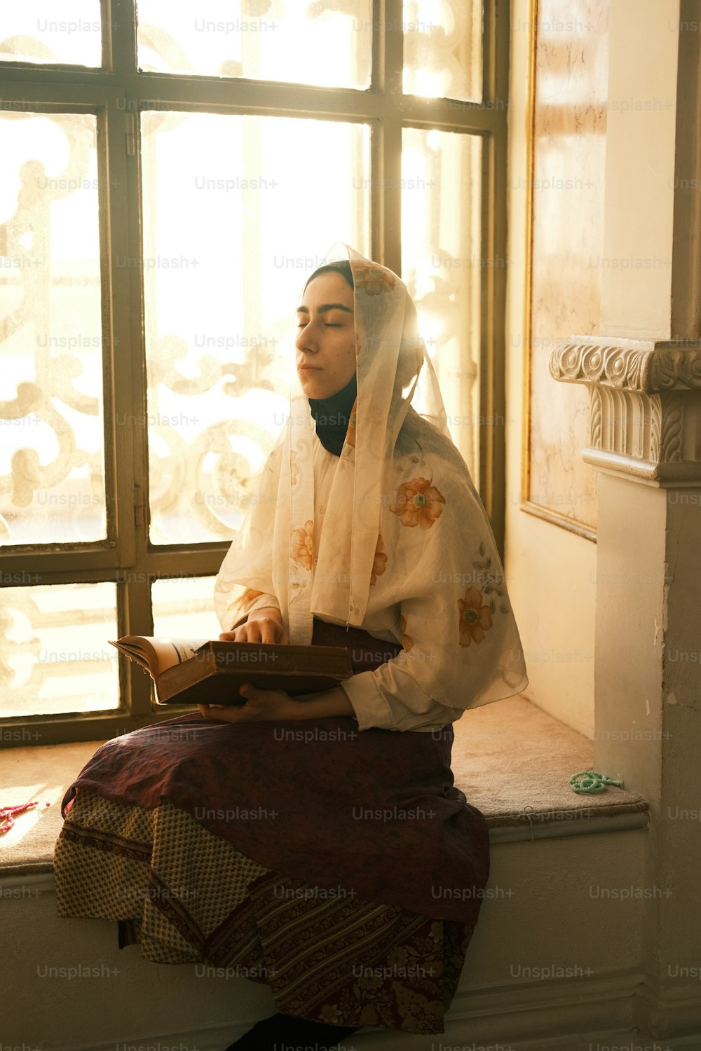 a woman sitting on a window sill reading a book