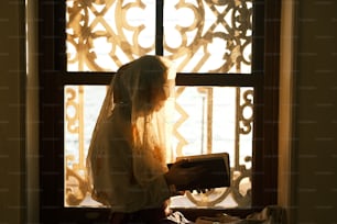 a woman standing in front of a window holding a book