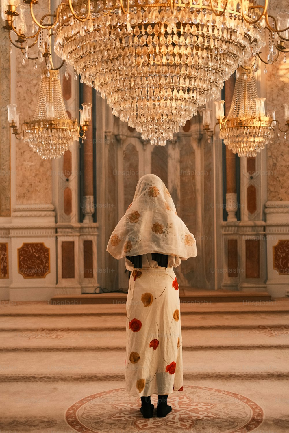 Una mujer con un vestido blanco de pie debajo de una lámpara de araña