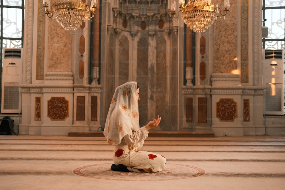 une mariée agenouillée sur le sol devant un lustre