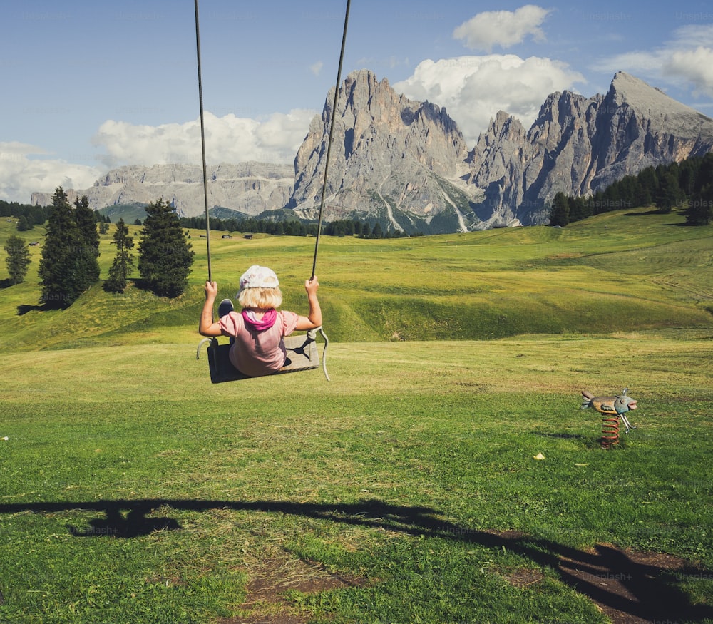 a little girl sitting on a swing in a field