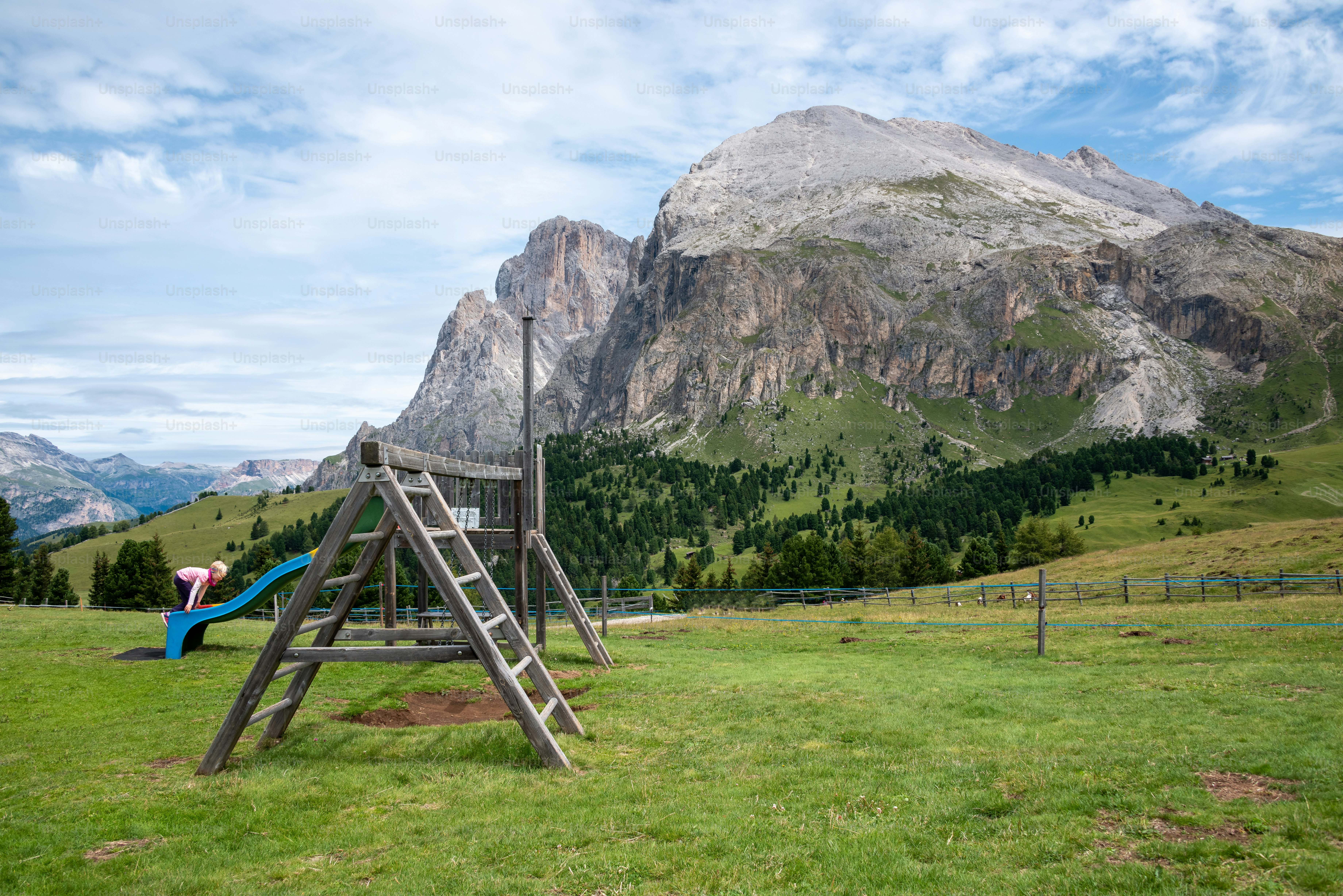 A wooden swing set in a grassy field with mountains in the background ...