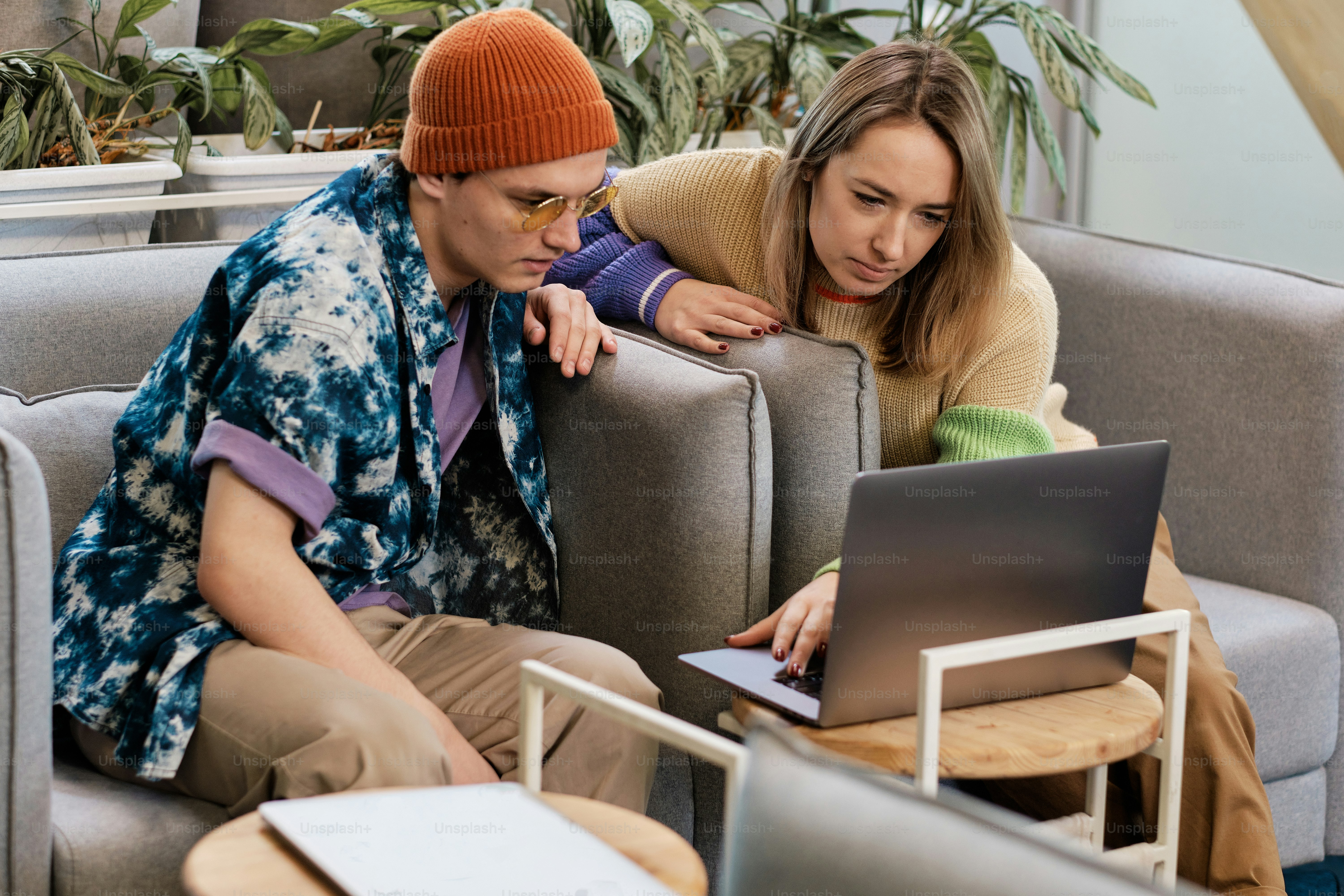 a man and a woman sitting on a couch looking at a laptop