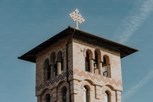 una alta torre de reloj de ladrillo con una cruz en la parte superior