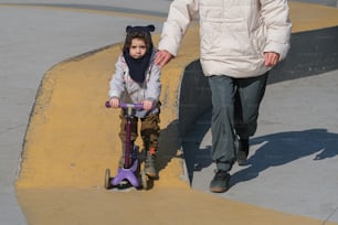 a little girl riding a scooter next to a man