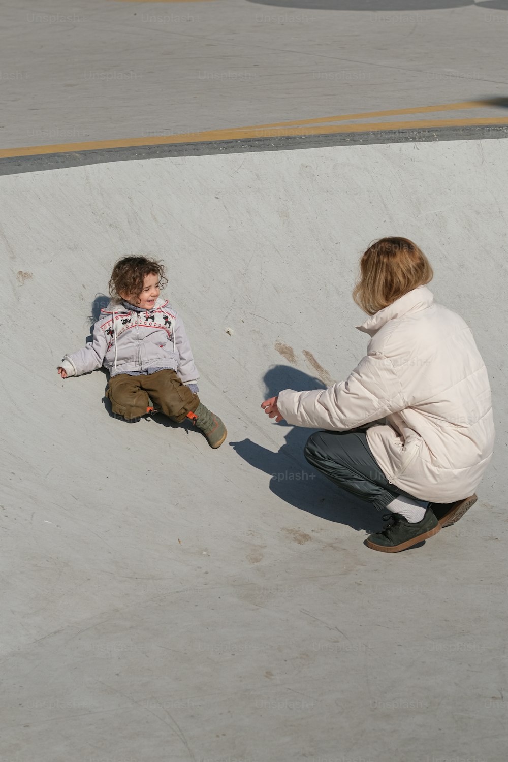 a woman kneeling down next to a child on a skateboard