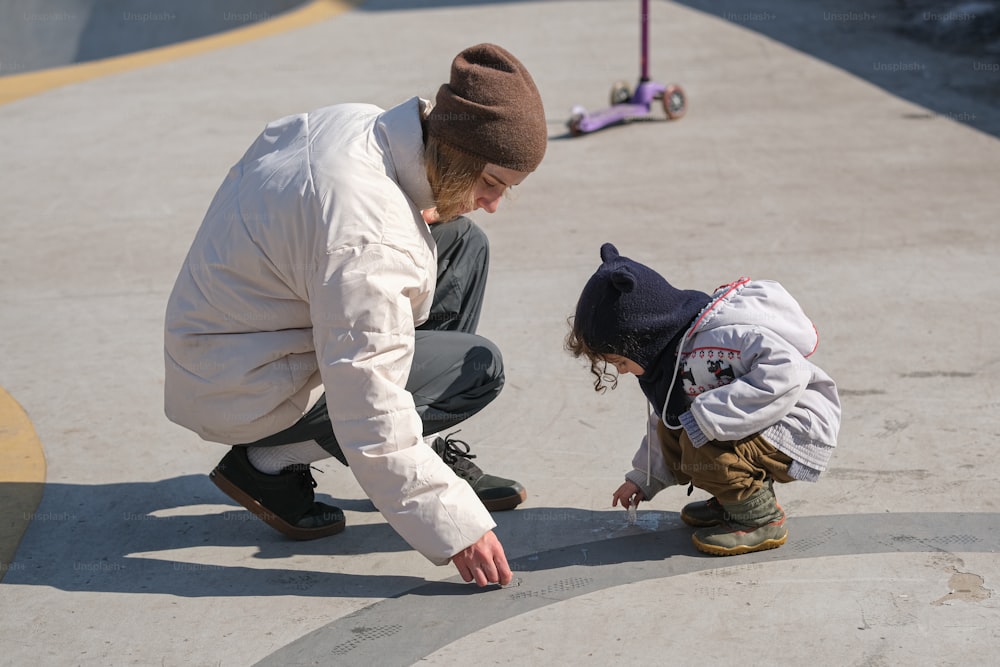 a man kneeling down next to a little girl on a skateboard