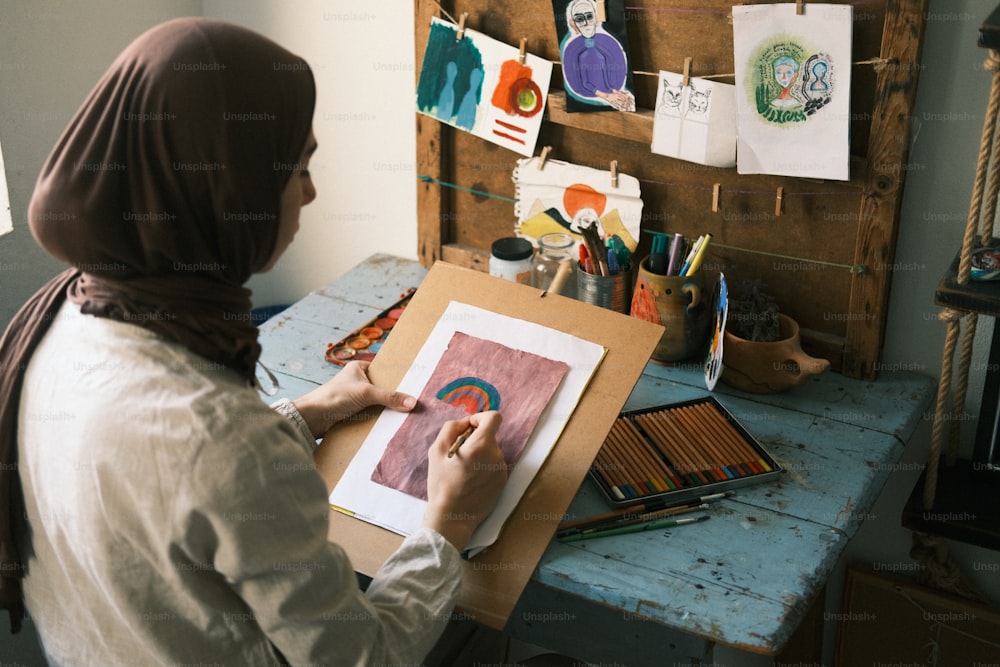 �ヒジャーブを着た女性が一枚の紙に絵を描いている