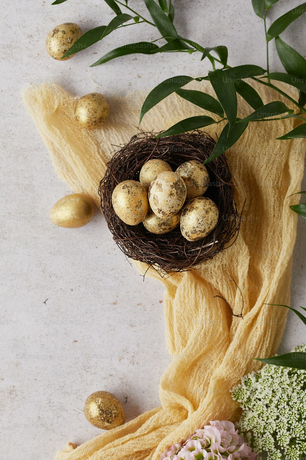 a bird's nest with eggs and flowers on a yellow cloth