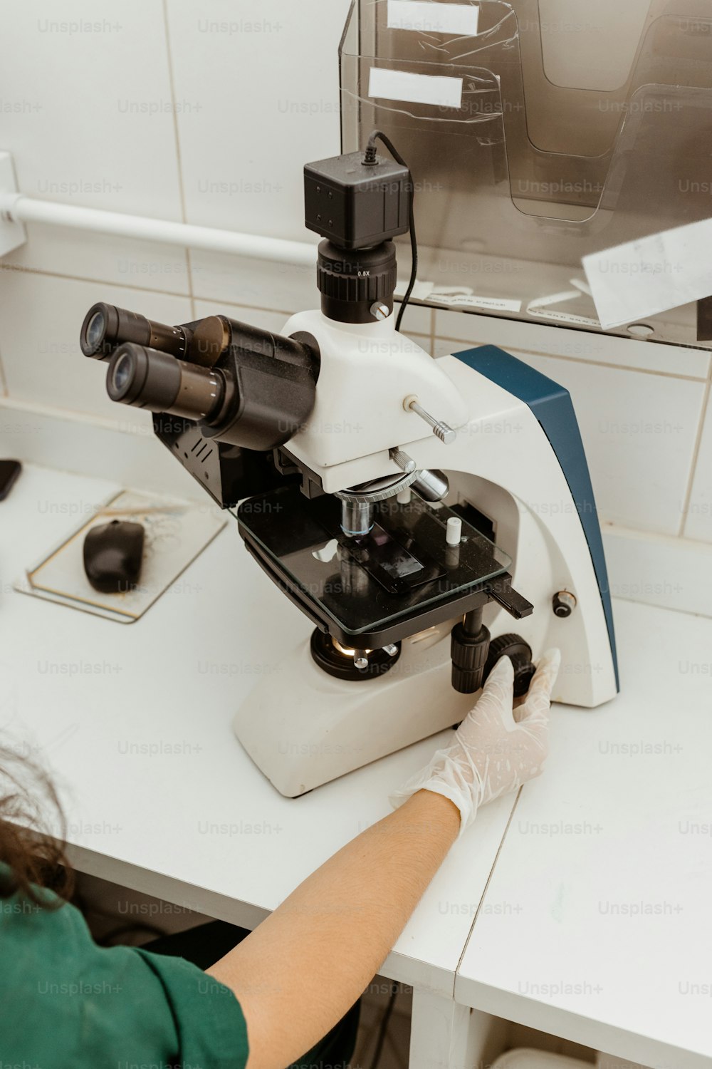 Una mujer con una camisa verde está mirando a través de un microscopio