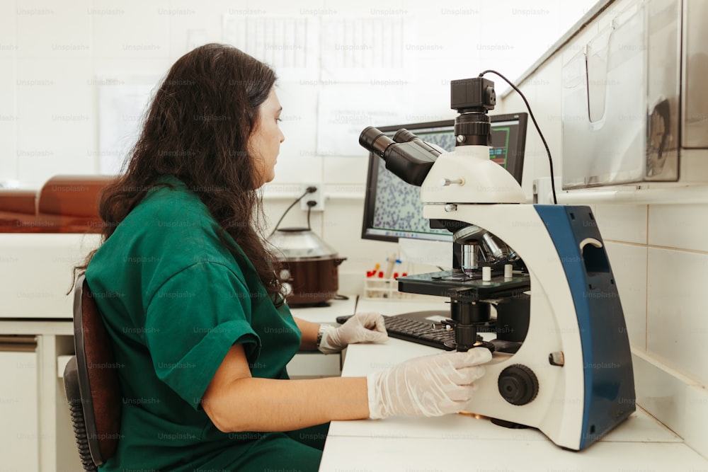 a woman in a green shirt is looking at a microscope