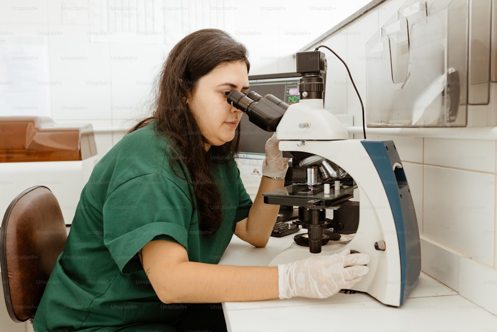 Eine Frau im grünen Hemd schaut durch ein Mikroskop
