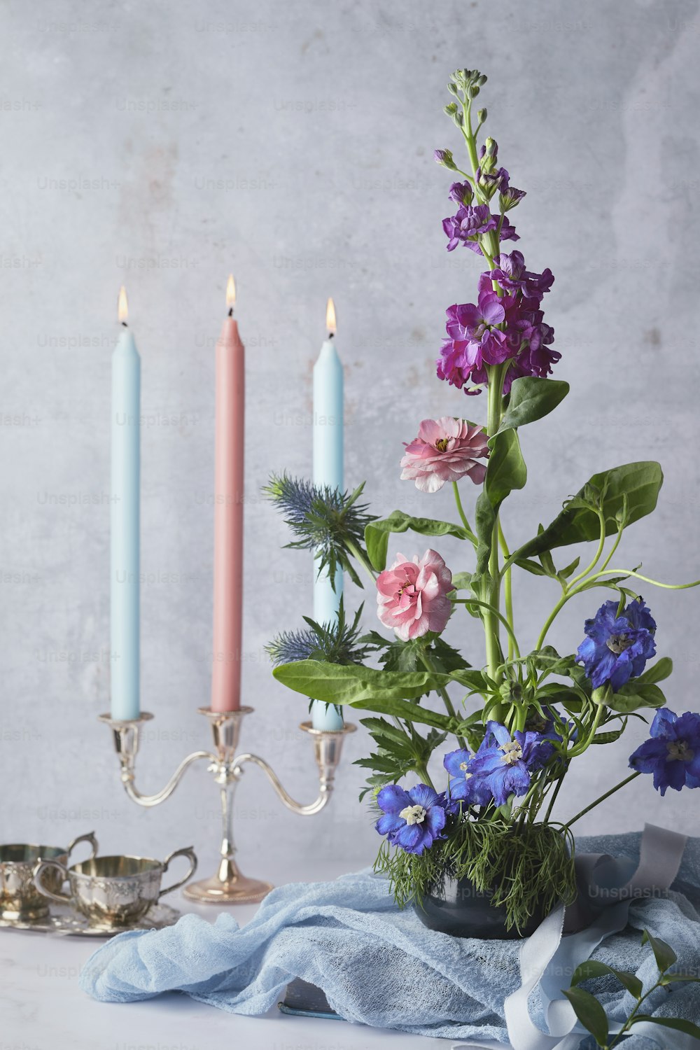 eine Vase gefüllt mit Blumen neben zwei Kerzen