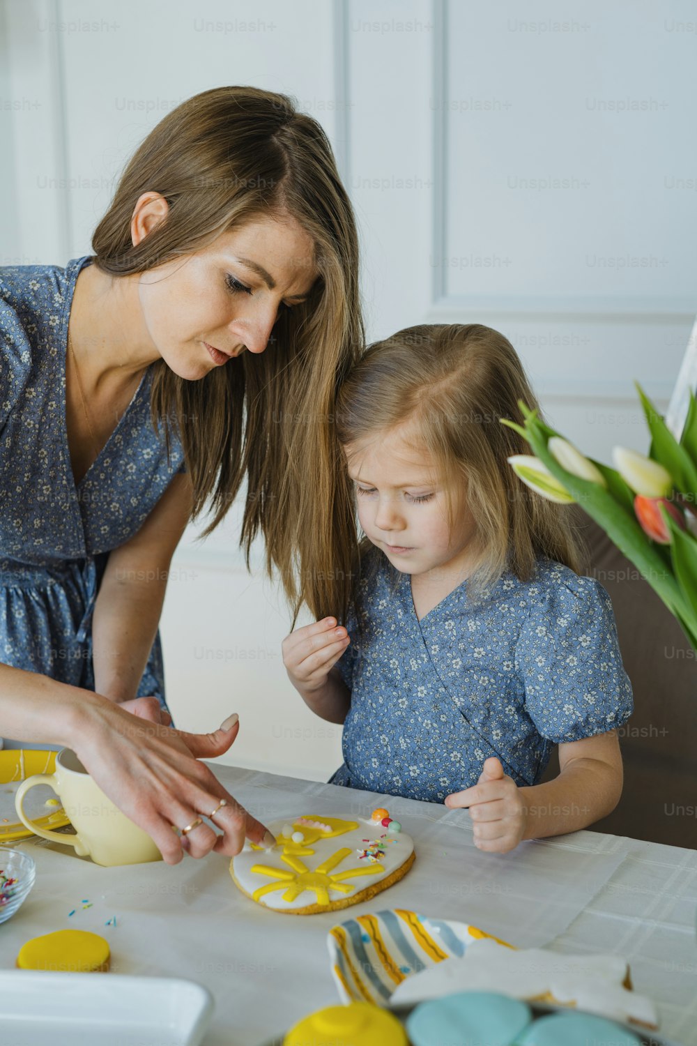 Una mujer ayudando a una niña a decorar un pastel
