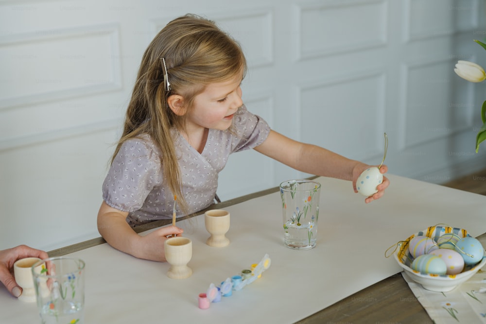 a little girl sitting at a table with some eggs
