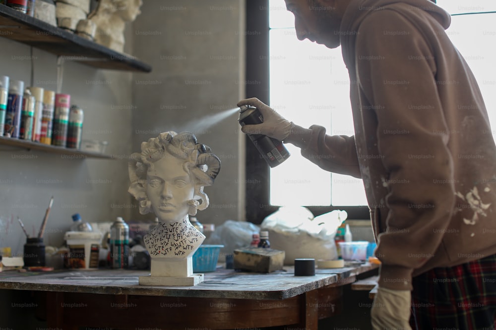 Un hombre pintando con aerosol una estatua de la cabeza de una mujer