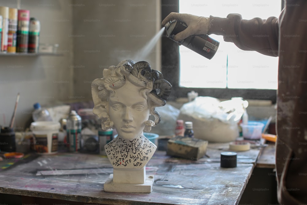 Una persona rociando pintura sobre un busto de una mujer