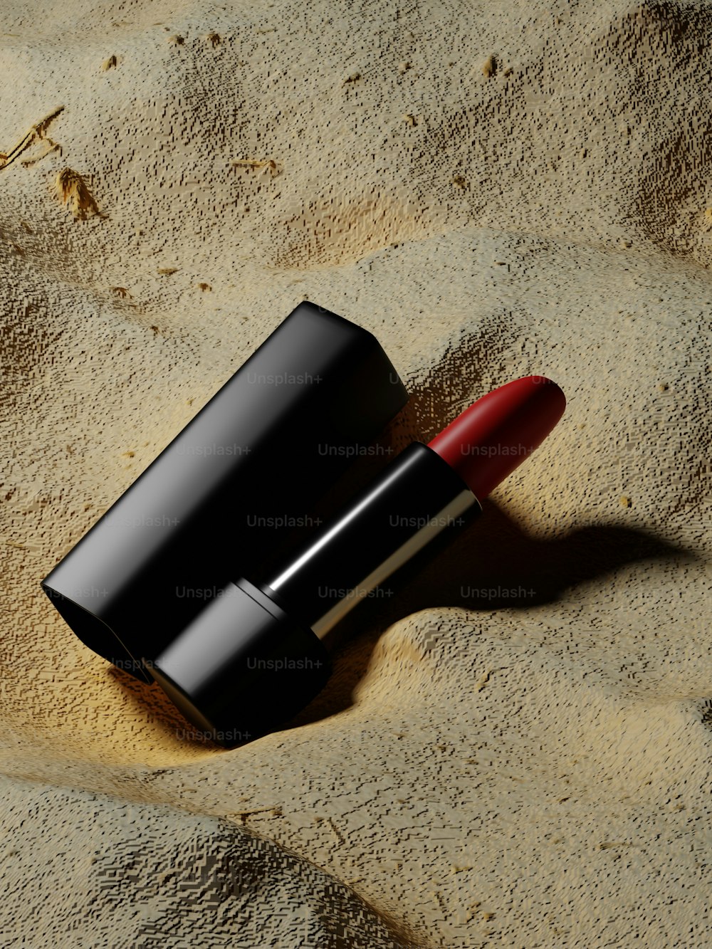 a red lipstick sitting on top of a sandy beach